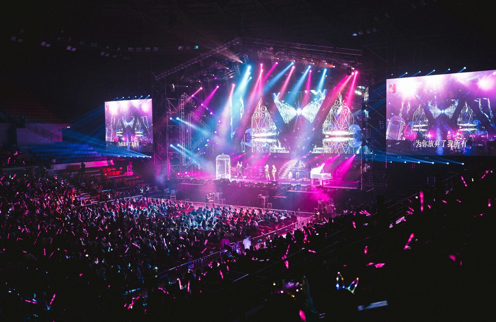 Arena lotada vista de cima durante um show, com o palco iluminado